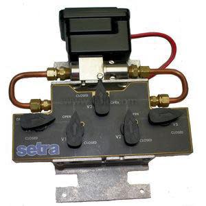 Pressure transmitter assembly featuring a black sensor block, loops of copper tubing and multiple valve knobs labeled open and closed