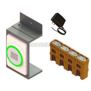 Illustration of a kit including a rectangular wall-mounted device with a glowing green ring on its face, a tan block with four battery slots, and a small black plug-in adapter.
