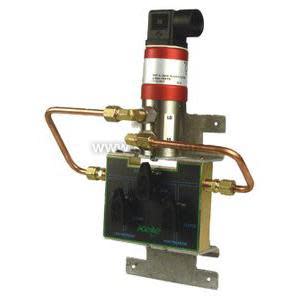Pressure control assembly featuring a transducer with red band on top, copper pipes and brass fittings mounted on a metal bracket