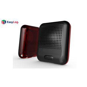 Square black device covered in tiny holes with a red translucent cover sitting nearby.