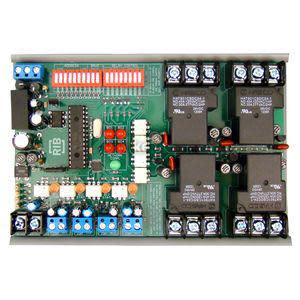 Rectangular circuit board with four large black relays, numerous screw terminals, DIP switch strip and electronic components