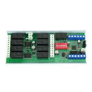 Long green printed circuit board containing several black relay modules, a red DIP switch block, and rows of connector pins and screw terminals